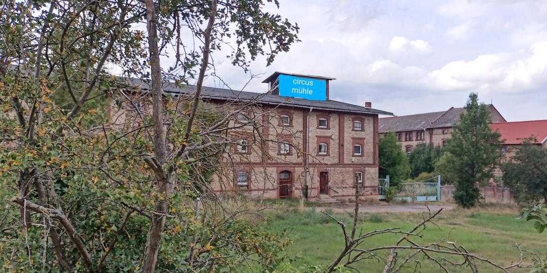 Ansicht eines ehemaligen Getreidespeichers und einer Wassermühle auf einer grünen Wiese. Alte Ziegelstein-Gebäude vor wolkigem Himmel.